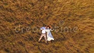 幸福<strong>的</strong>新婚夫妇躺在一片黄色<strong>的</strong>草地上。 空中飞行。 从上面看。 背景草地上美丽<strong>的</strong>年轻夫妇